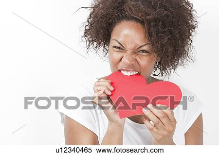 Portrait of frustrated young African American woman biting heart shape against white background View Large Photo Image Stock Photography - Portrait of frustrated young African American woman biting heart shape against white background. Fotosearch