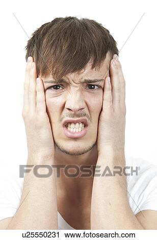 Stock Image - Portrait of frustrated young man clenching teeth against white background. Fotosearch
