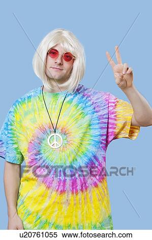 Stock Photography - Portrait of funky young man gesturing peace sign against blue background. Fotosearch