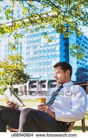 Portrait of handsome businessman drinking coffee and reading newspaper while sitting on folding chair in park View Large Photo Image Picture - Portrait of handsome businessman drinking coffee and reading newspaper while sitting on folding chair in park. Fotosearch