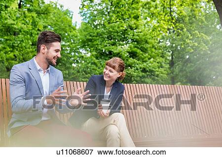 Portrait of handsome businessman gesturing and talking to businesswoman while sitting on bench during office break View Large Photo Image Stock Photo - Portrait of handsome businessman gesturing and talking to businesswoman while sitting on bench during office break. Fotosearch