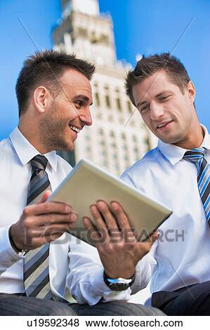 Stock Photo - Portrait of handsome businessman showing business plan to the other businessman over digital tablet while sitting. Fotosearch