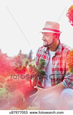 Portrait of handsome gardener wearing hat while holding flower pot in the garden View Large Photo Image Stock Image - Portrait of handsome gardener wearing hat while holding flower pot in the garden. Fotosearch