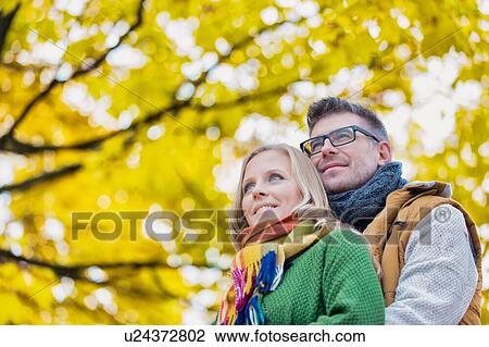 Stock Image - Portrait of handsome man embracing his wife from the back in park. Fotosearch