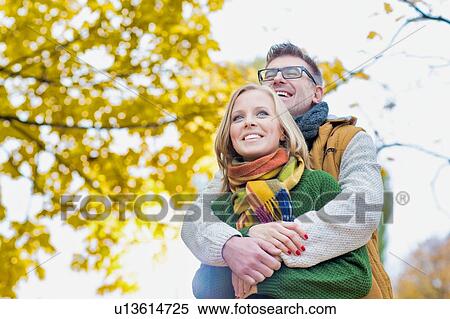 Stock Photography - Portrait of handsome man embracing his wife from the back in park. Fotosearch