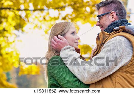 Stock Image - Portrait of handsome man showing affection to his wife in park. Fotosearch