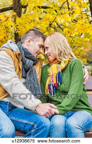 Stock Photography - Portrait of handsome man sitting while showing affection to his beautiful wife in park. Fotosearch