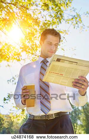 Stock Photo - Portrait of handsome mature businessman holding cup of coffee while reading newspaper in park during break . Fotosearch