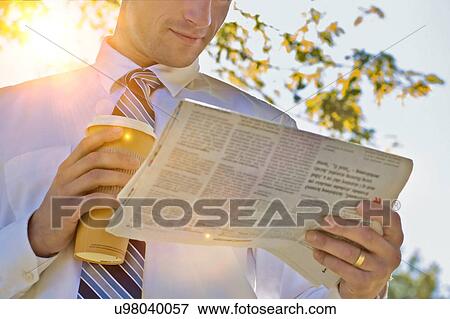 Portrait of handsome mature businessman holding cup of coffee while reading newspaper in park during break View Large Photo Image Stock Photo - Portrait of handsome mature businessman holding cup of coffee while reading newspaper in park during break . Fotosearch