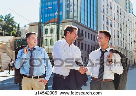 Stock Photograph - Portrait of handsome mature businessman shaking hands with colleague after meeting against office building. Fotosearch