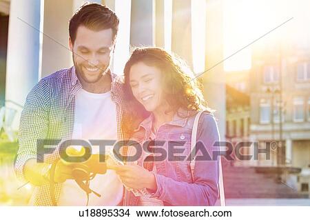 Portrait of handsome young man showing pictures on camera to his beautiful girlfriend while sitting against museum with lens flare in background View Large Photo Image Picture - Portrait of handsome young man showing pictures on camera to his beautiful girlfriend while sitting against museum with lens flare in background. Fotosearch