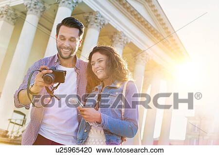 Portrait of handsome young man showing pictures on camera to his beautiful girlfriend while sitting against museum with lens flare in background View Large Photo Image Stock Image - Portrait of handsome young man showing pictures on camera to his beautiful girlfriend while sitting against museum with lens flare in background. Fotosearch