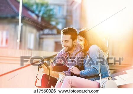 Portrait of handsome young man showing pictures on camera to his beautiful girlfriend while sitting against museum with lens flare in background View Large Photo Image Stock Photograph - Portrait of handsome young man showing pictures on camera to his beautiful girlfriend while sitting against museum with lens flare in background. Fotosearch