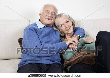 Portrait of happy elderly man with arm around spouse sitting on sofa at home View Large Photo Image Stock Photography - Portrait of happy elderly man with arm around spouse sitting on sofa at home. Fotosearch