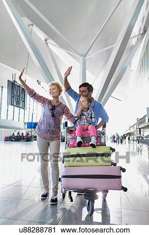 Stock Image - Portrait of happy family waving in arrival area at airport. Fotosearch