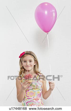 Portrait of happy girl holding cupcake and party balloon over colored background View Large Photo Image Stock Photo - Portrait of happy girl holding cupcake and party balloon over colored background. Fotosearch