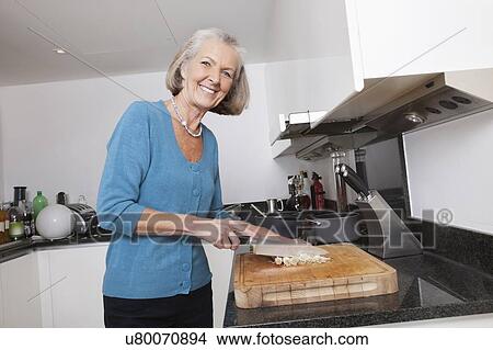 Picture - Portrait of happy senior woman chopping vegetables at kitchen counter. Fotosearch