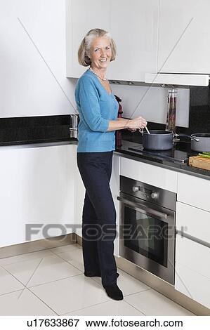 Stock Photo - Portrait of happy senior woman preparing food in kitchen. Fotosearch