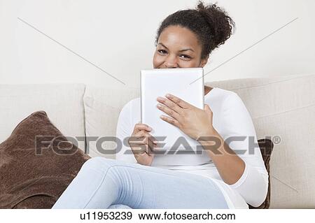 Portrait of happy young African American woman holding tablet PC on sofa View Large Photo Image Stock Photo - Portrait of happy young African American woman holding tablet PC on sofa. Fotosearch