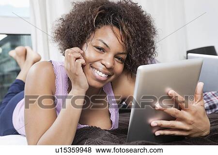 Stock Photo - Portrait of happy young African American woman using tablet PC in bed. Fotosearch