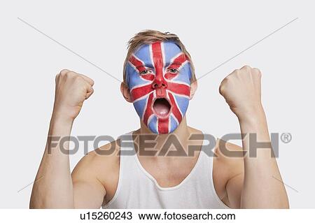 Stock Image - Portrait of happy young Caucasian man with British flag painted on face celebrating success against white background. Fotosearch