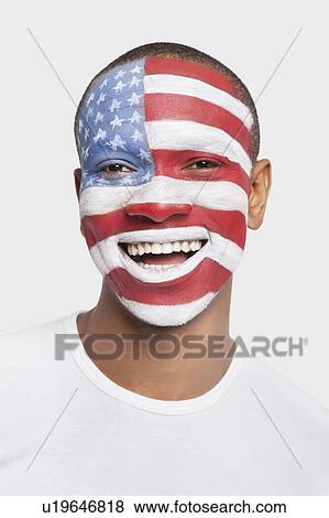 Stock Photo - Portrait of happy young Hispanic man with North American flag painted on face against white background. Fotosearch