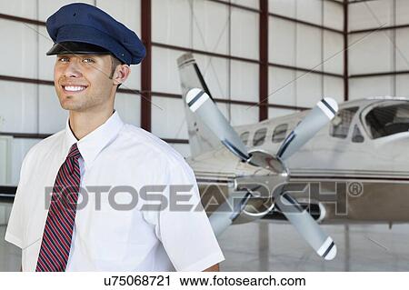 Stock Image - Portrait of happy young male pilot standing in front of airplane. Fotosearch