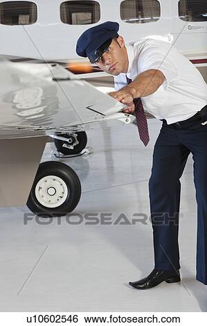 Stock Photograph - Portrait of happy young male pilot inspecting airplane's wing. Fotosearch