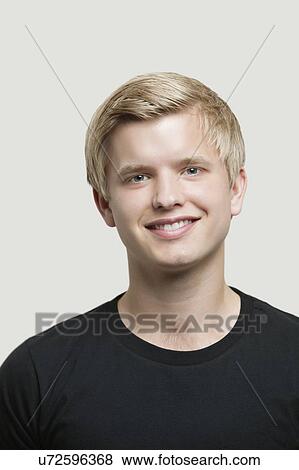Stock Photo - Portrait of happy young man against gray background. Fotosearch