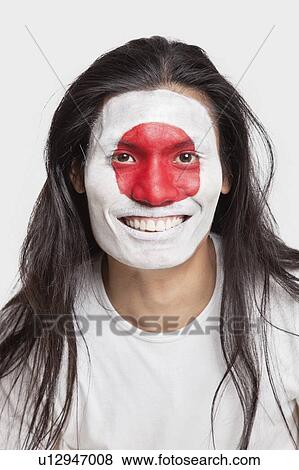 Stock Photo - Portrait of happy young man with long hair and Japanese flag painted on face against white background. Fotosearch