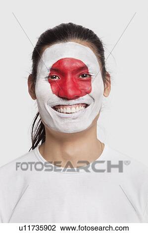 Stock Image - Portrait of happy young mixed race man with Japanese flag painted on face against white background. Fotosearch