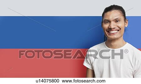 Stock Image - Portrait of happy young mixed race man standing against French flag. Fotosearch