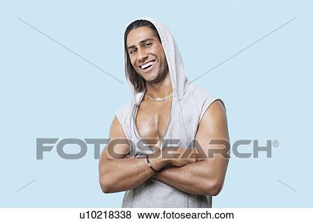 Stock Photo - Portrait of happy young muscular man with arms crossed standing against blue background. Fotosearch