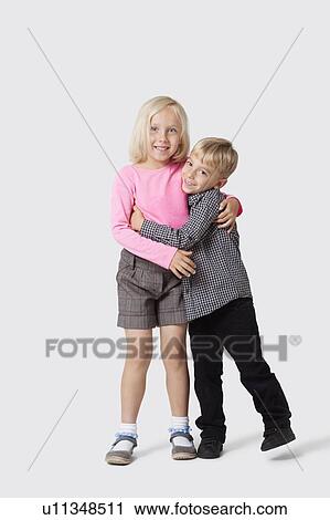 Stock Image - Portrait of happy young siblings hugging over white background. Fotosearch
