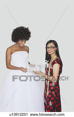 Portrait of Indian female designer assisting African American bride with feather fascinator over gray background View Large Photo Image Stock Image - Portrait of Indian female designer assisting African American bride with feather fascinator over gray background. Fotosearch