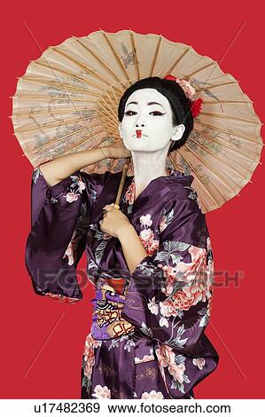 Portrait of Japanese woman in kimono holding parasol against red background View Large Photo Image Stock Photo - Portrait of Japanese woman in kimono holding parasol against red background. Fotosearch