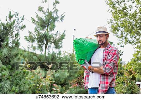 Stock Image - Portrait of male gardener carrying sack of soil on his shoulder while walking in garden shop. Fotosearch
