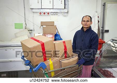 Stock Image - Portrait of male worker with shopping cart in store. Fotosearch