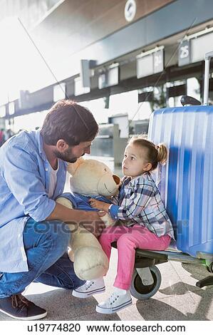 Stock Image - Portrait of man holding teddy bear and playing with his daughter in check in area at airport. Fotosearch