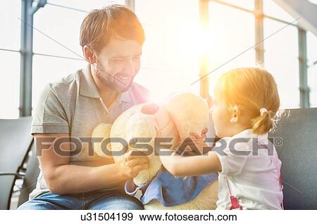 Stock Photo - Portrait of man playing with her daughter while sitting and waiting for boarding in airport. Fotosearch