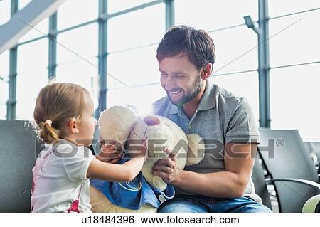 Stock Photograph - Portrait of man playing with her daughter while sitting and waiting for boarding in airport. Fotosearch