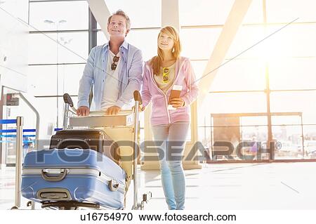 Stock Image - Portrait of man pushing baggage cart for check in with her daughter at airport. Fotosearch
