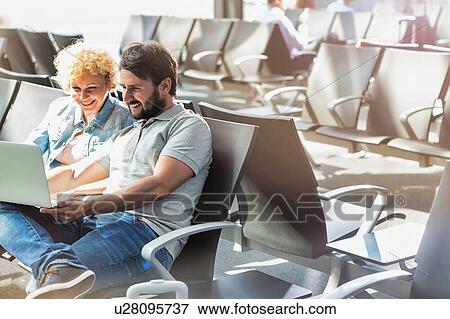 Stock Photo - Portrait of man showing funny picture with his wife while waiting in airport. Fotosearch