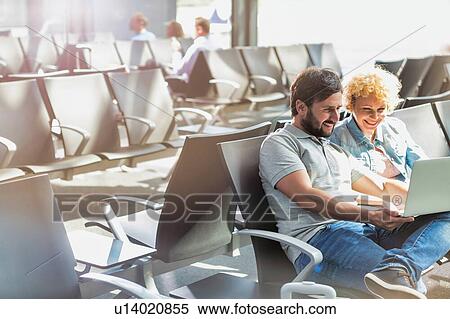 Stock Photography - Portrait of man showing funny picture with his wife while waiting in airport. Fotosearch