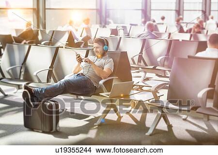 Portrait of man using smartphone with headphones on while waiting for boarding in airport View Large Photo Image Picture - Portrait of man using smartphone with headphones on while waiting for boarding in airport. Fotosearch