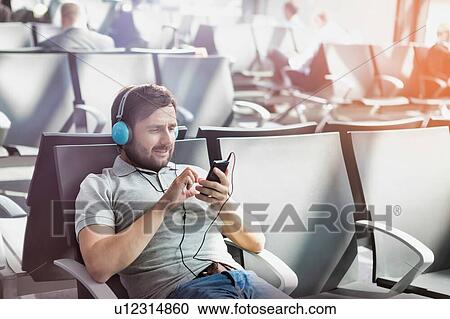 Stock Image - Portrait of man using smartphone with headphones on while waiting for boarding in airport. Fotosearch