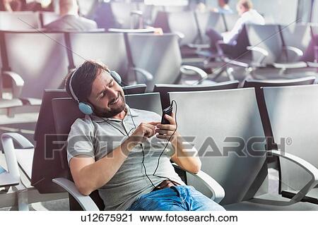 Stock Image - Portrait of man using smartphone with headphones on while waiting for boarding in airport. Fotosearch
