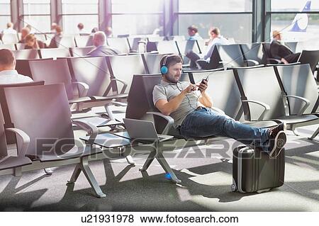 Stock Photo - Portrait of man using smartphone with headphones on while waiting for boarding in airport. Fotosearch