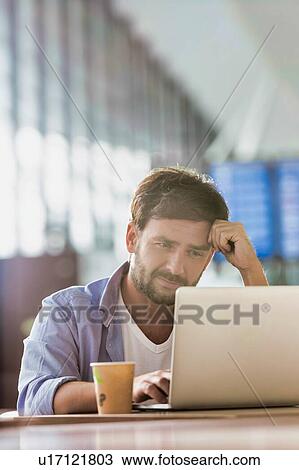 Stock Image - Portrait of man working with his laptop in cafe at airport while waiting for his flight. Fotosearch