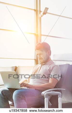 Stock Photo - Portrait of man working with his laptop while waiting for boarding in airport. Fotosearch